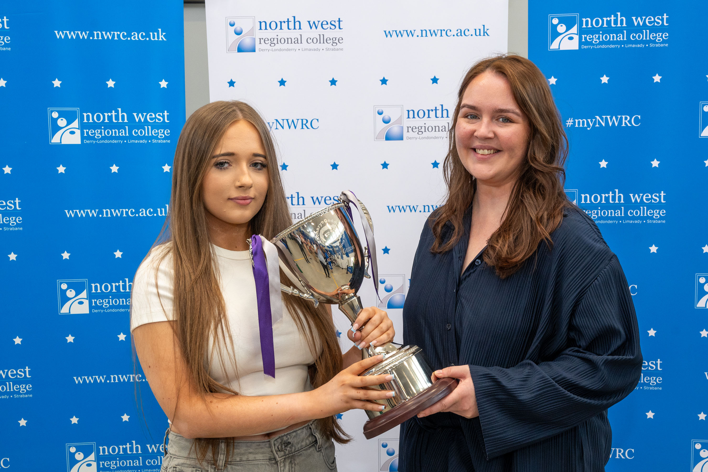 Two people at celebration event. One is presenting a trophy.