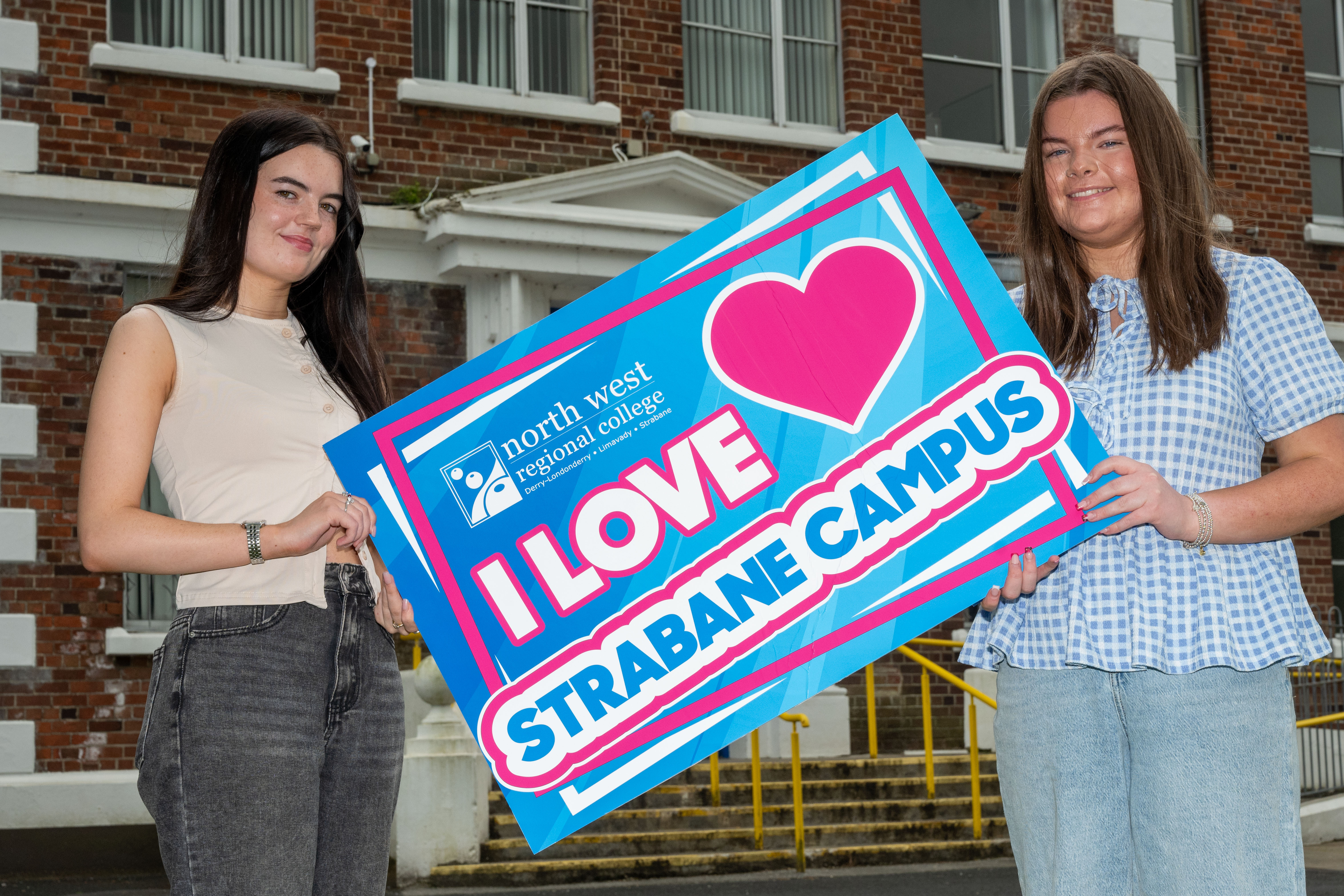 two students outside a college building holding a sign that says I love Strabane campus