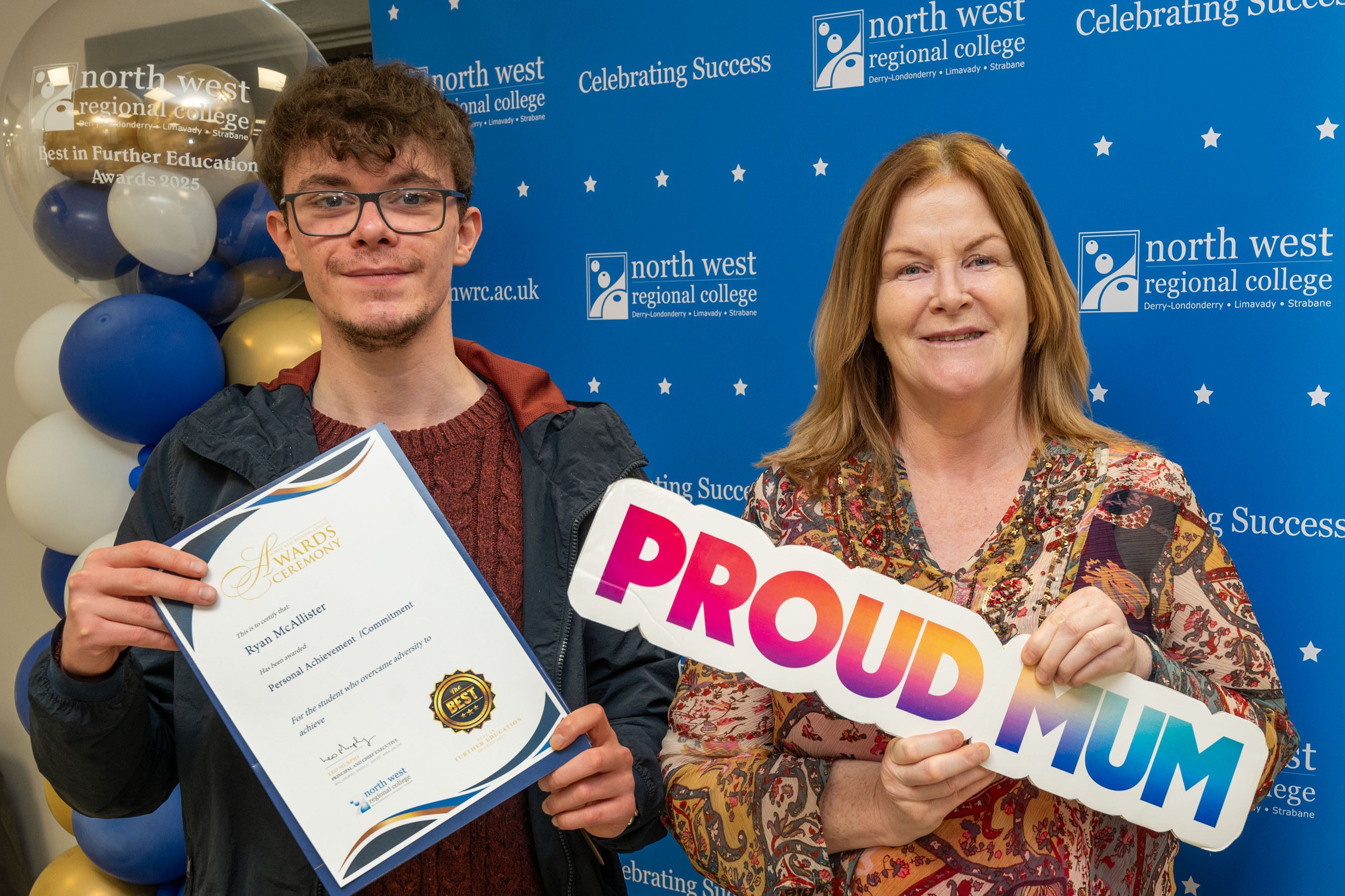 Two people at celebration event. One is holding a sign that says proud mum