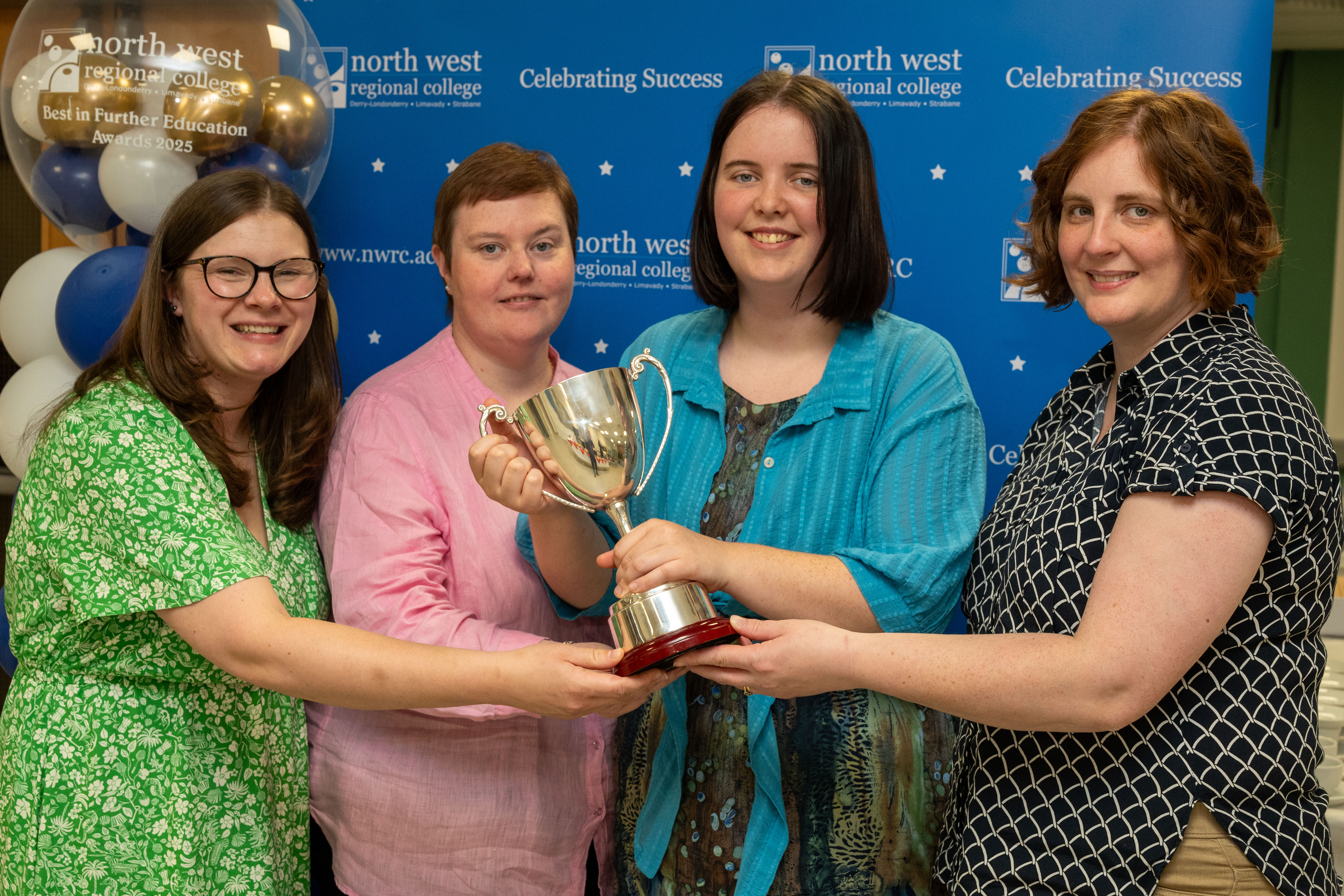 Four people at celebration event. One is holding a trophy