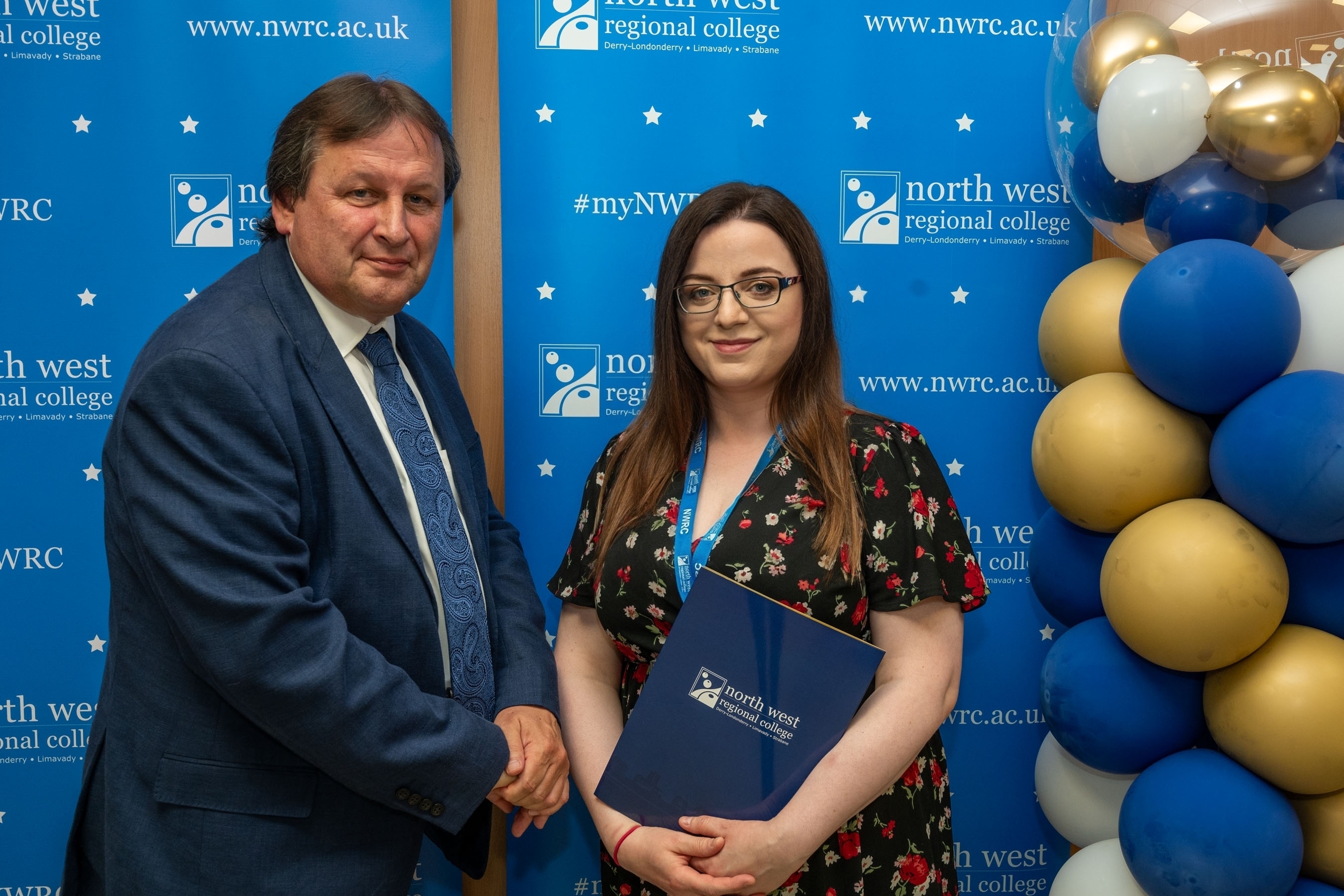 Man and woman in front of a NWRC blue screen holding a presentation holder.