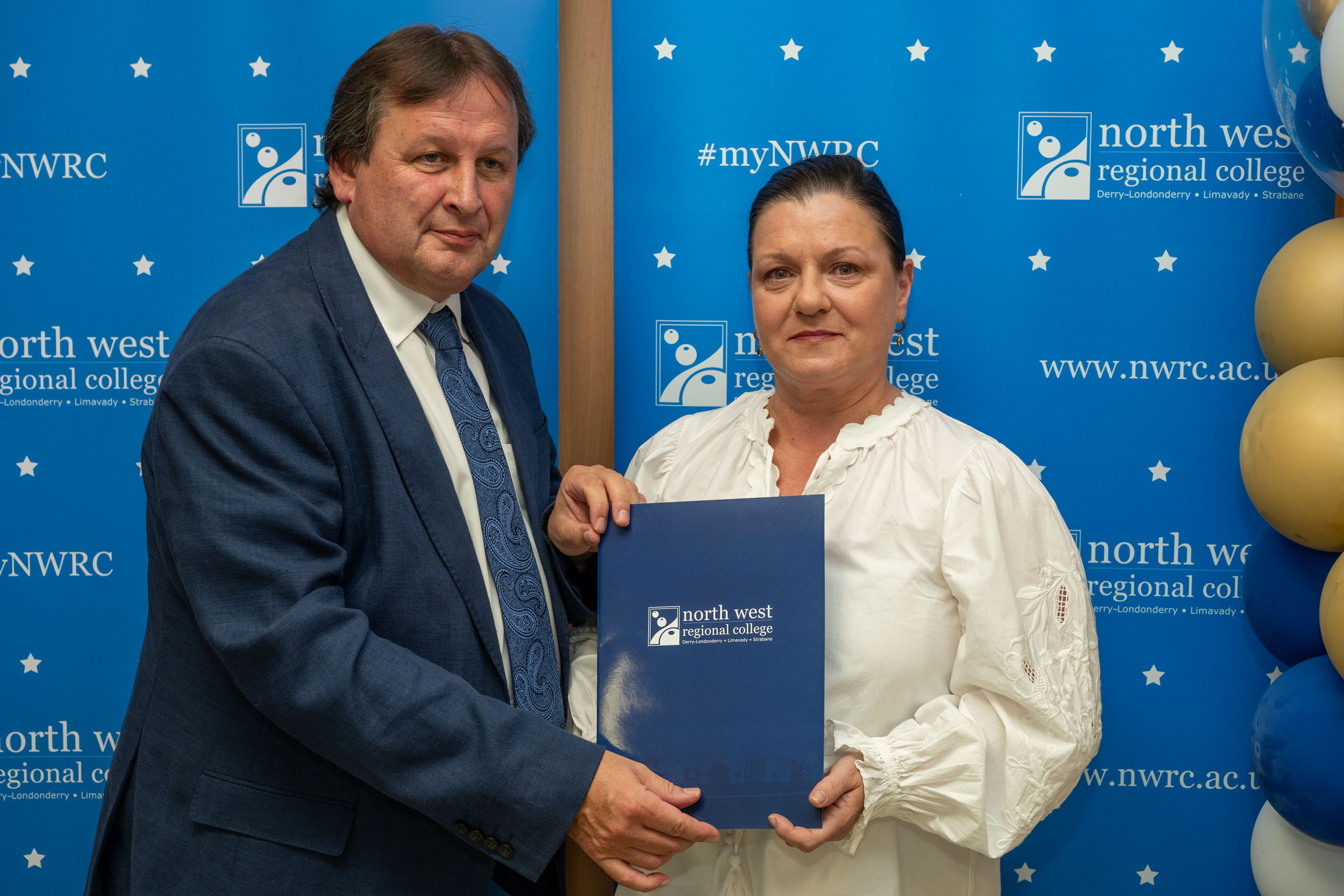 Man and woman in front of a NWRC blue screen holding a presentation holder.