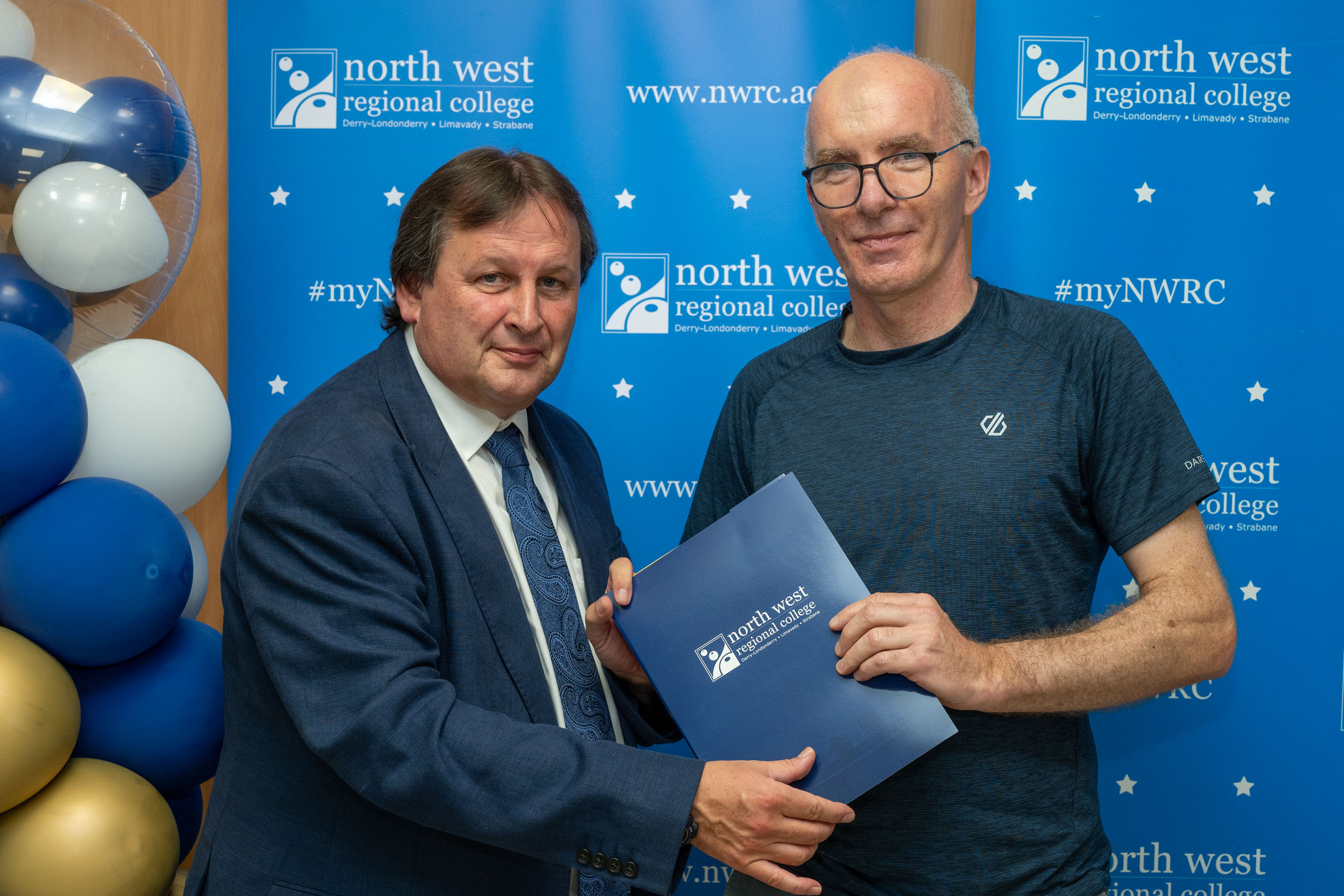 Two men in front of a NWRC blue screen holding a presentation holder.