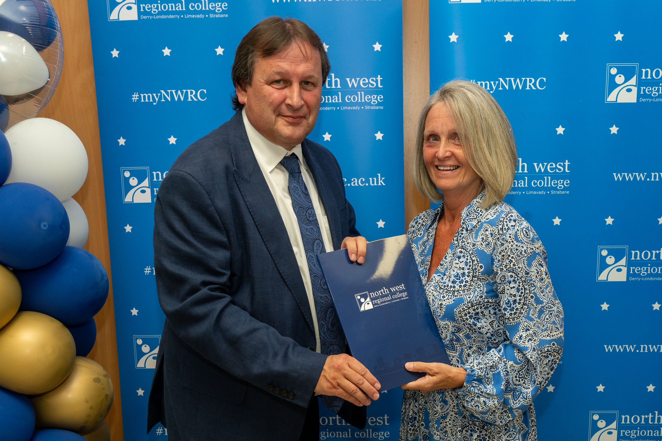 Man and woman in front of a NWRC blue screen holding a presentation holder.