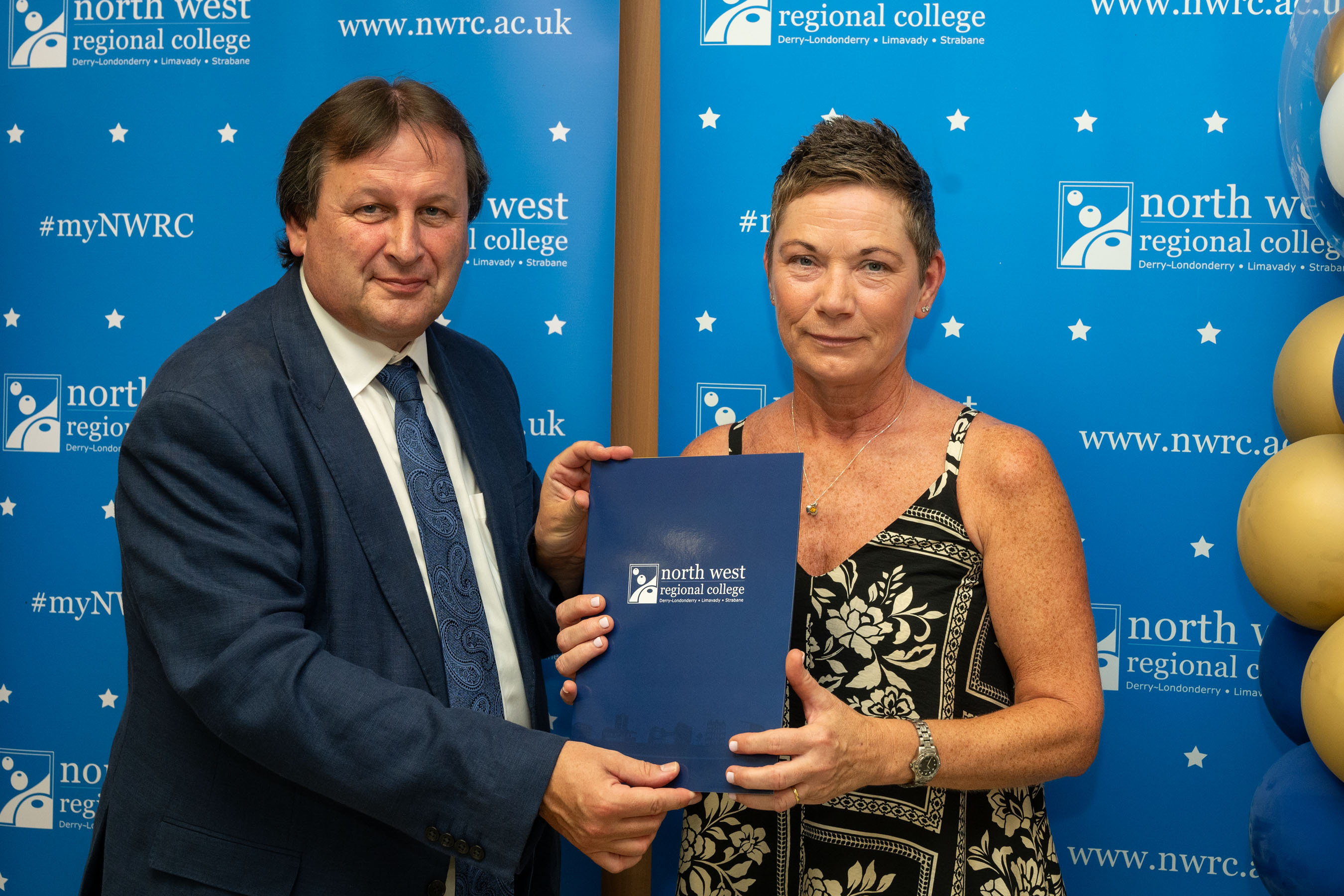 Man and woman in front of a NWRC blue screen holding a presentation holder.