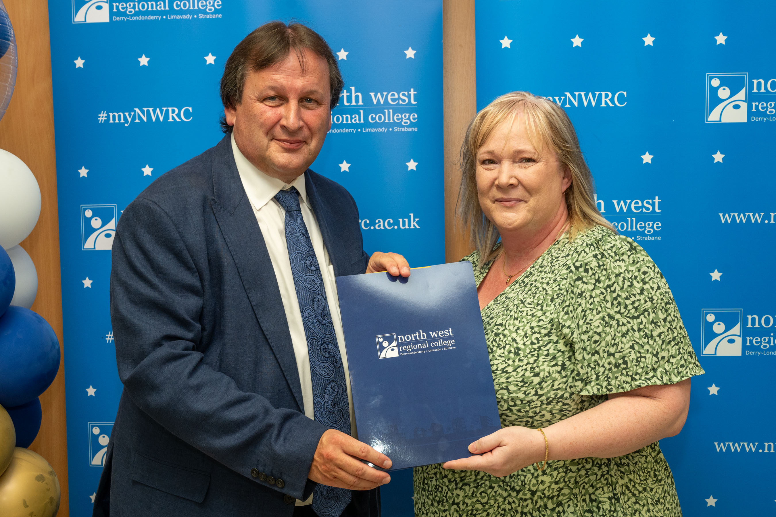 Man and woman in front of a NWRC blue screen holding a presentation holder.