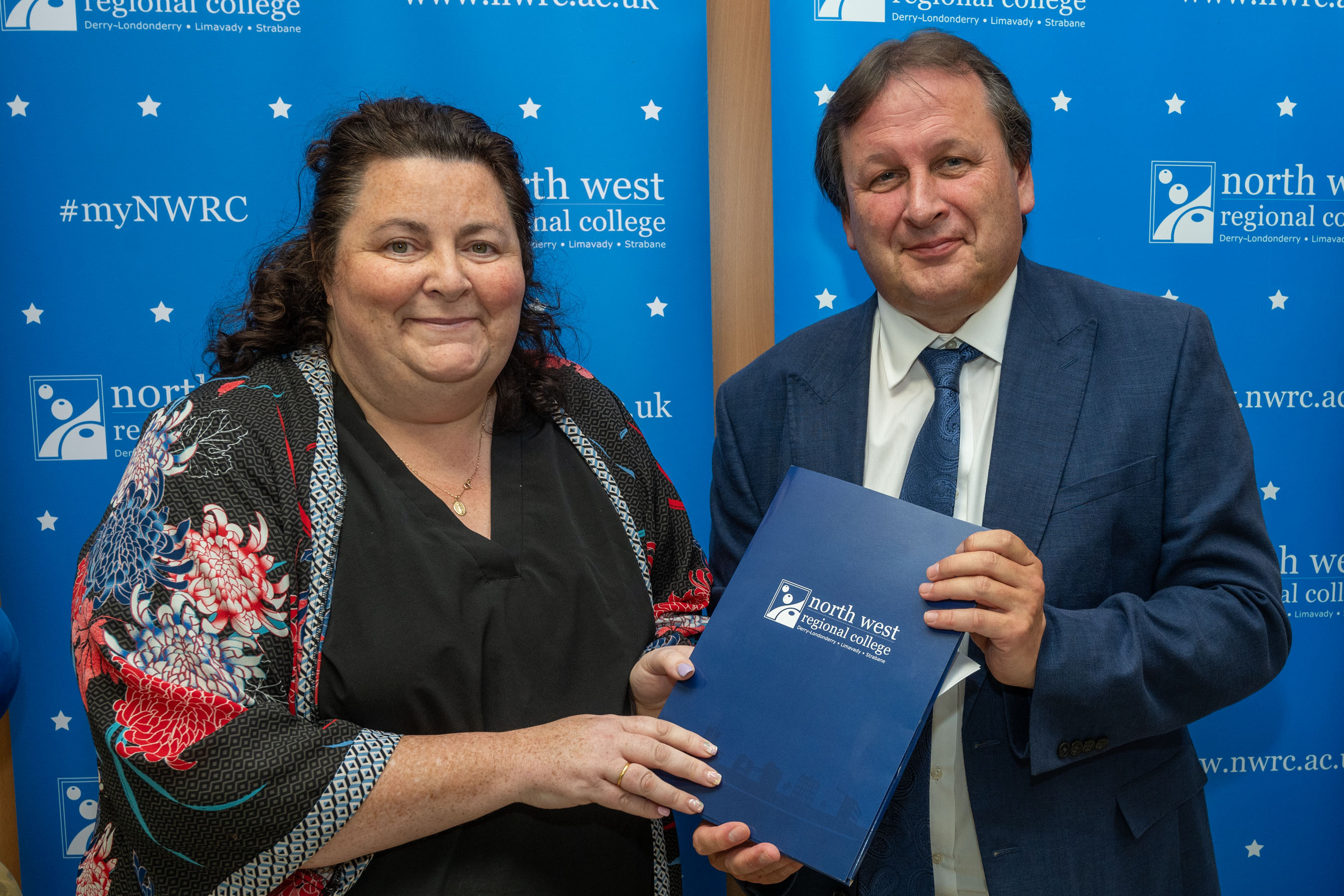 Man and woman in front of a NWRC blue screen holding a presentation holder.