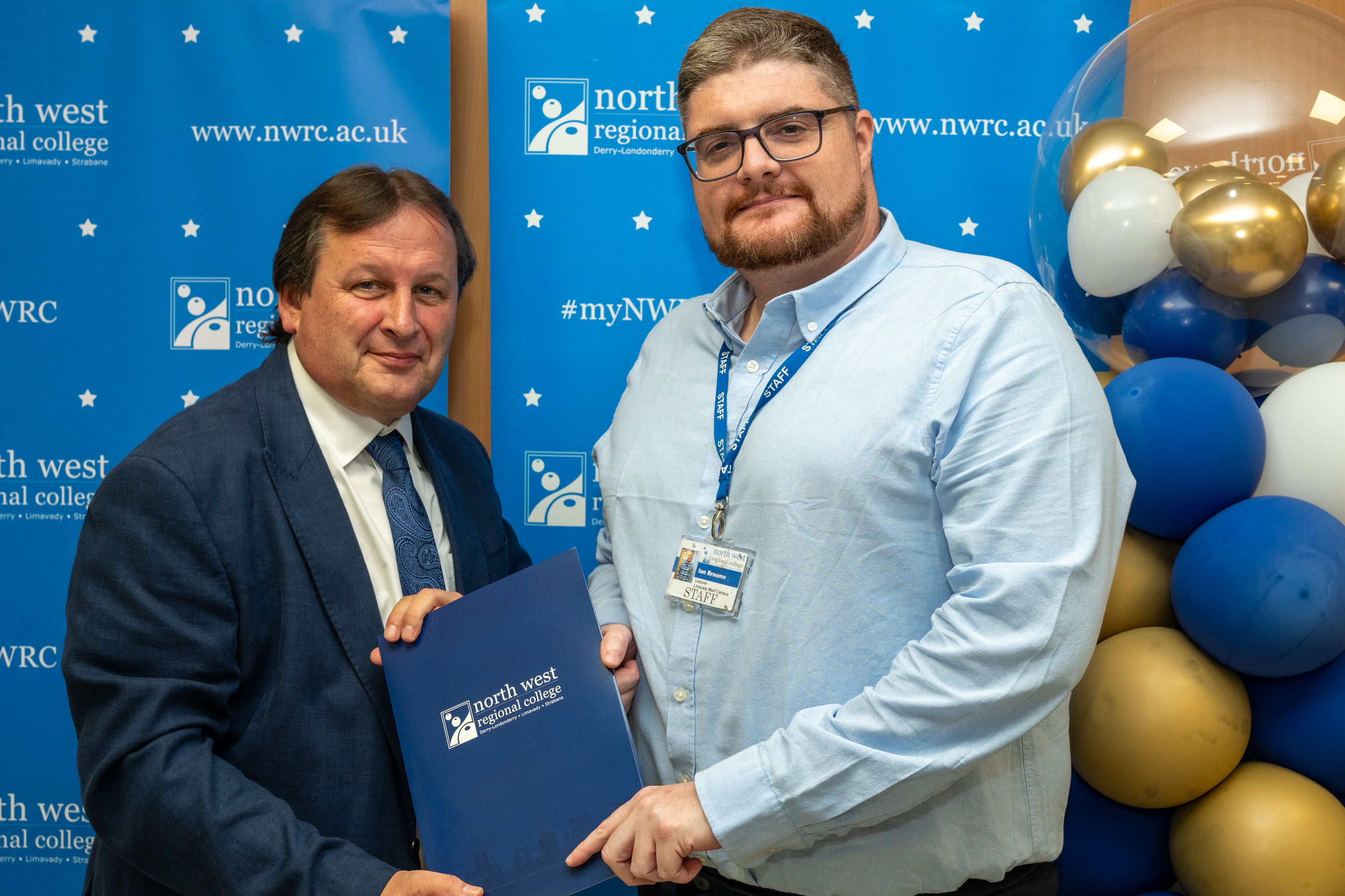 Two men in front of a NWRC blue screen holding a presentation holder.