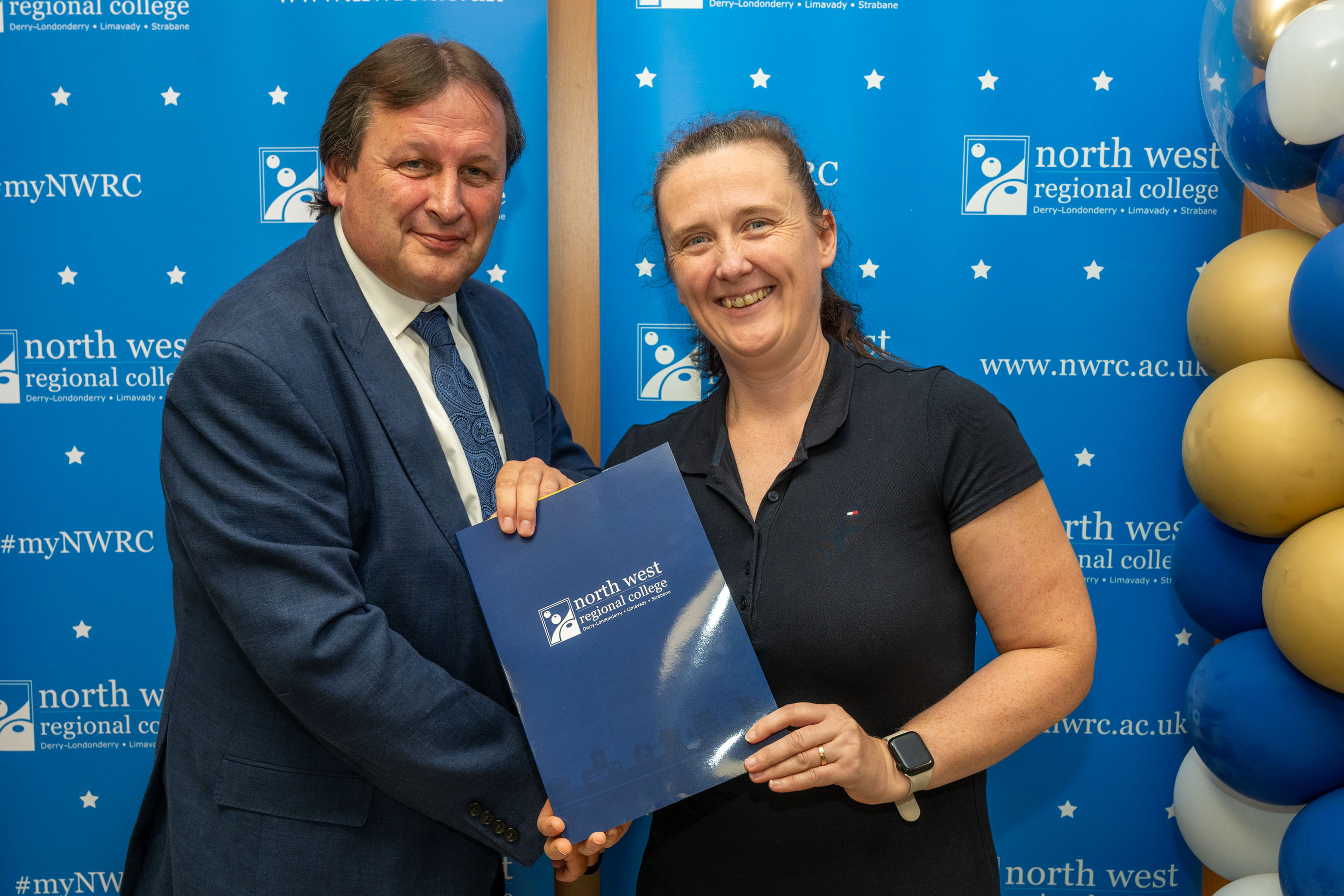 Man and woman in front of a NWRC blue screen holding a presentation holder.