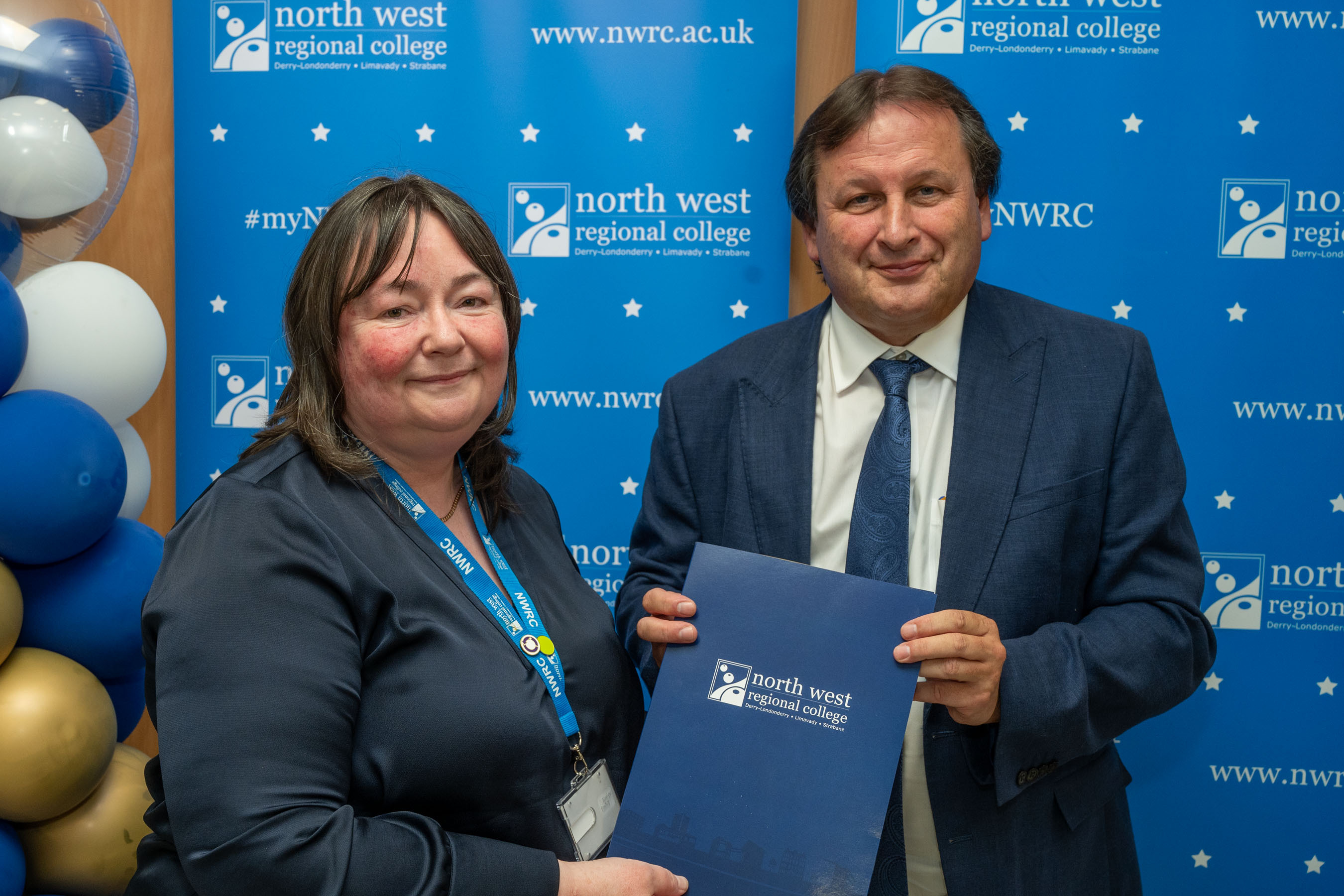 Man and woman in front of a NWRC blue screen holding a presentation holder.