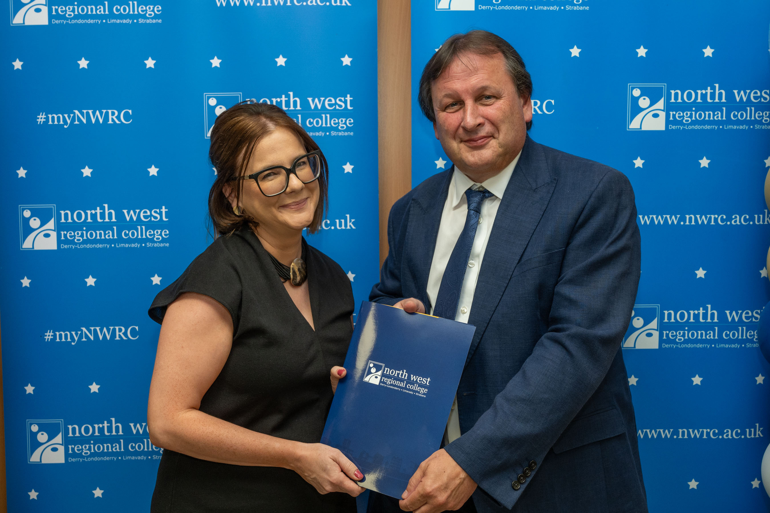 Man and woman in front of a NWRC blue screen holding a presentation holder.