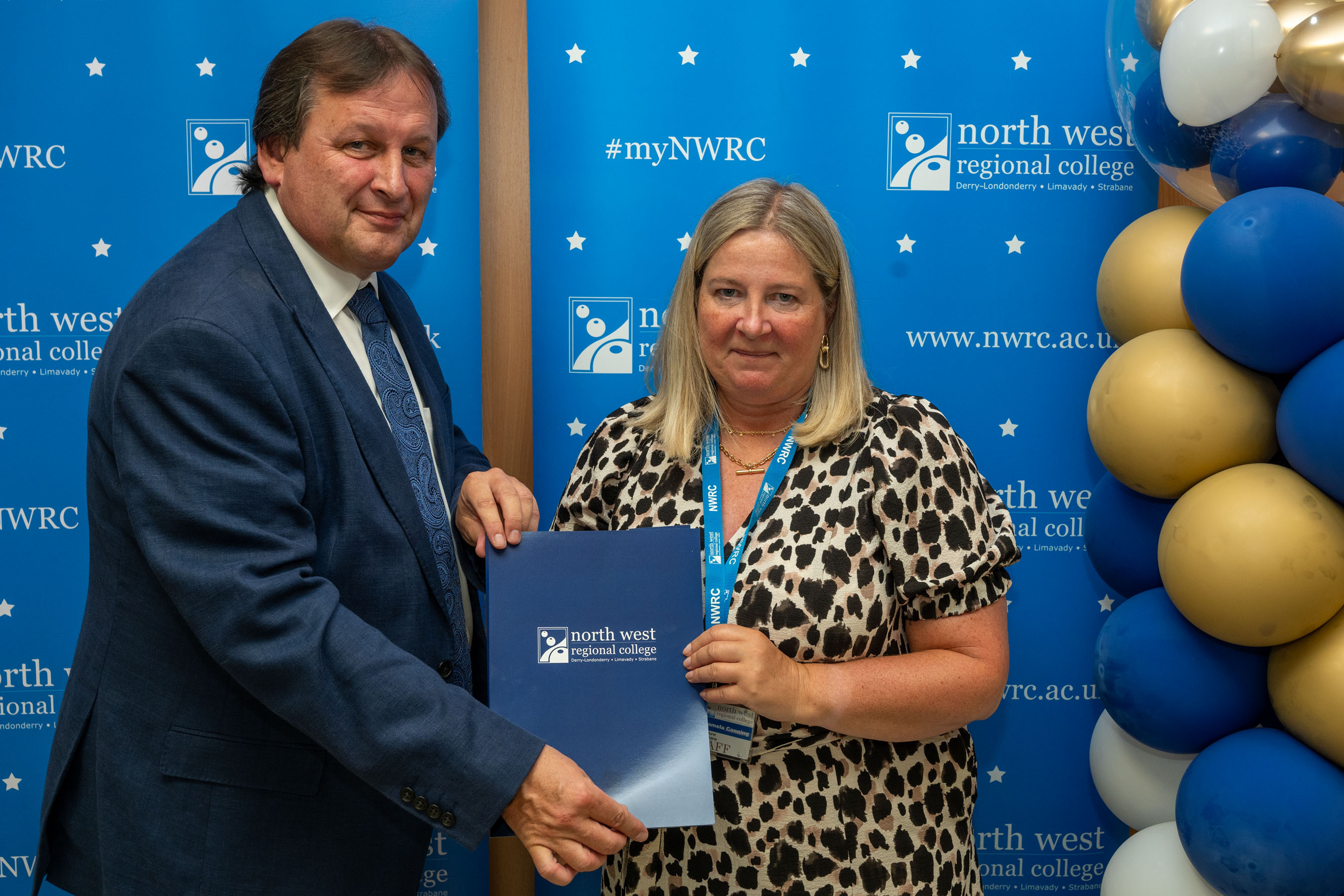 Man and woman in front of a NWRC blue screen holding a presentation holder.