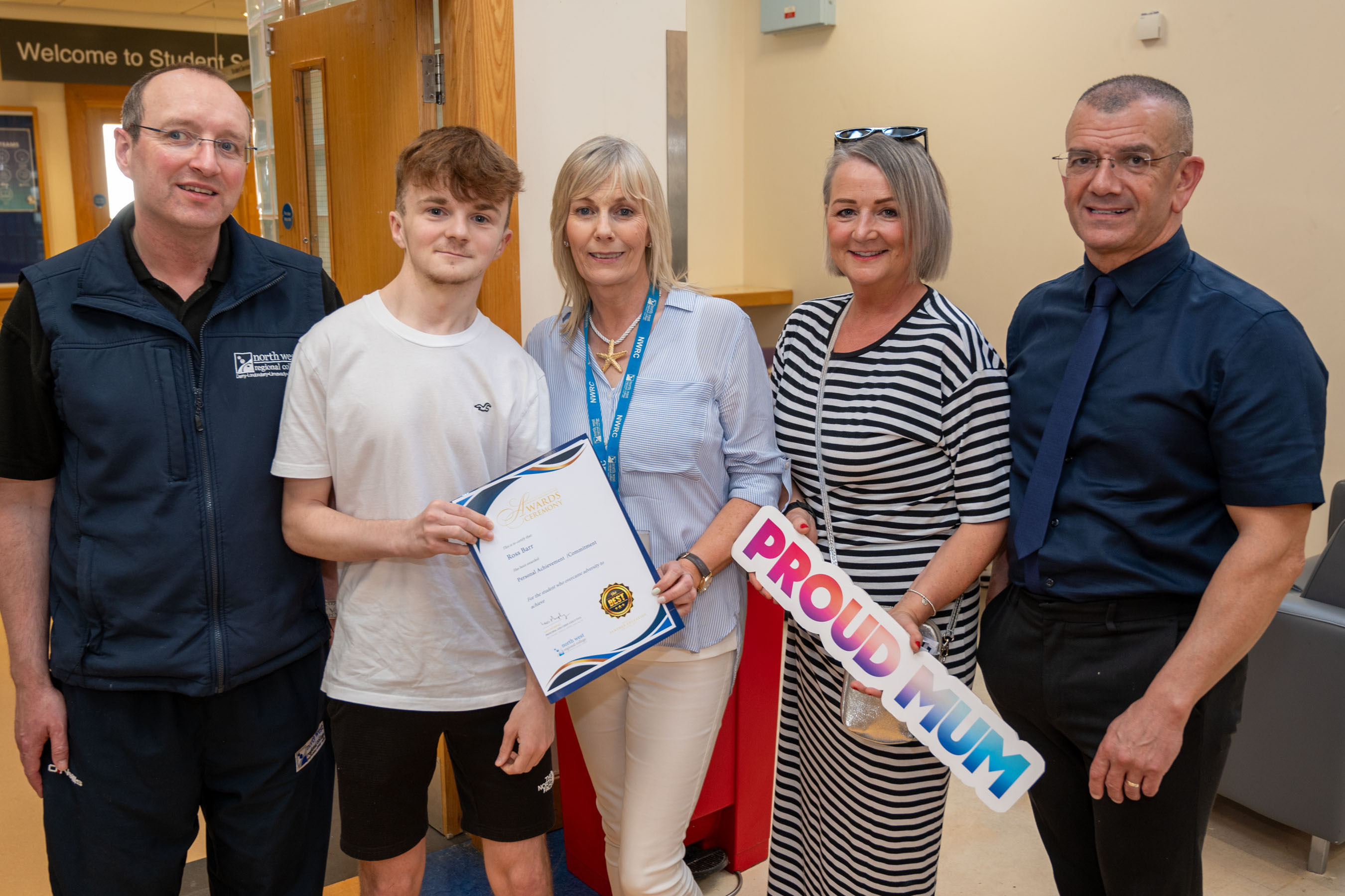 Five people at celebration event. One is holding a certificate, one has a proud mum sign.