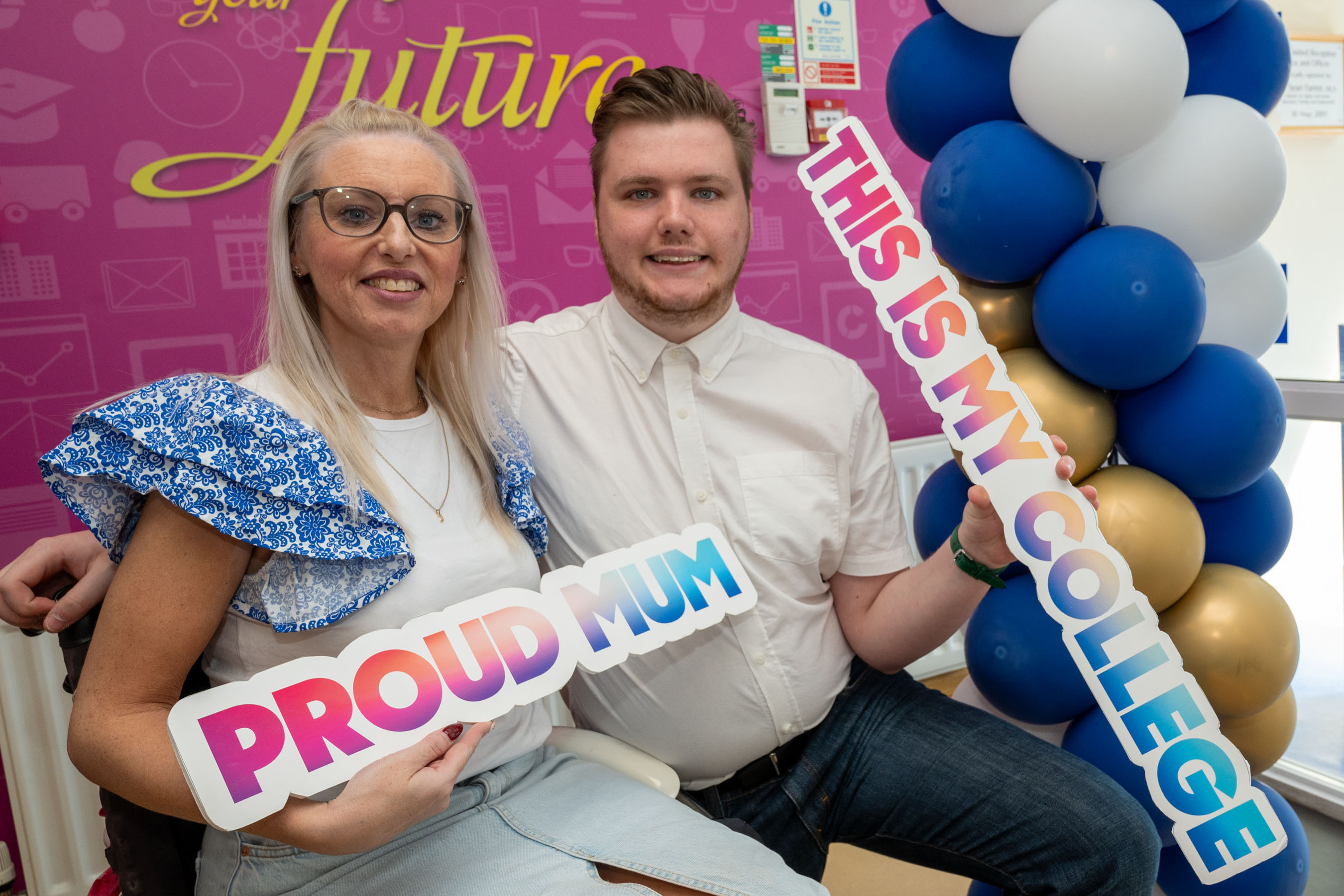 Two people at celebration event. One has a proud mum sign.