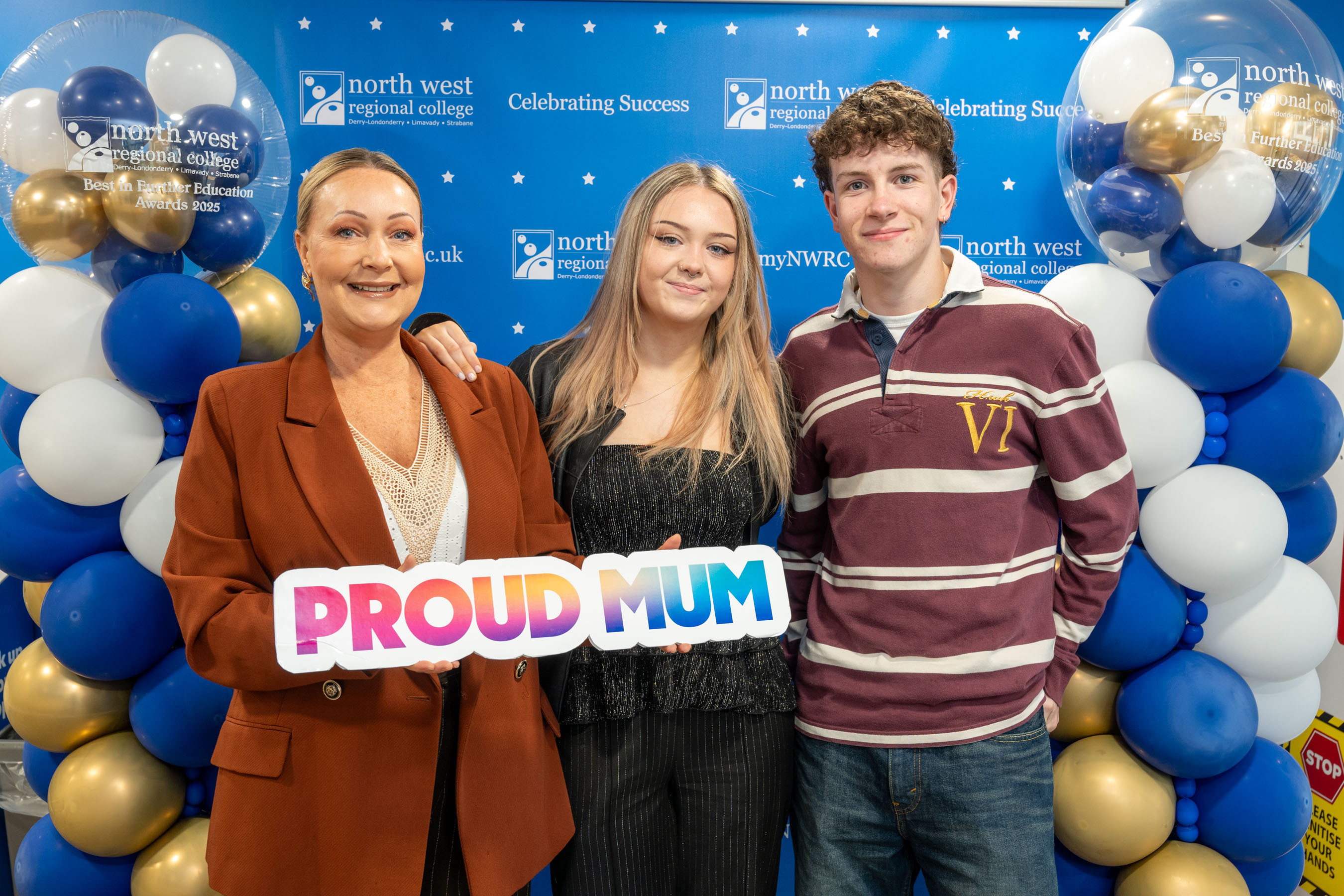 Three people at celebration event. Onehas a proud mum sign.