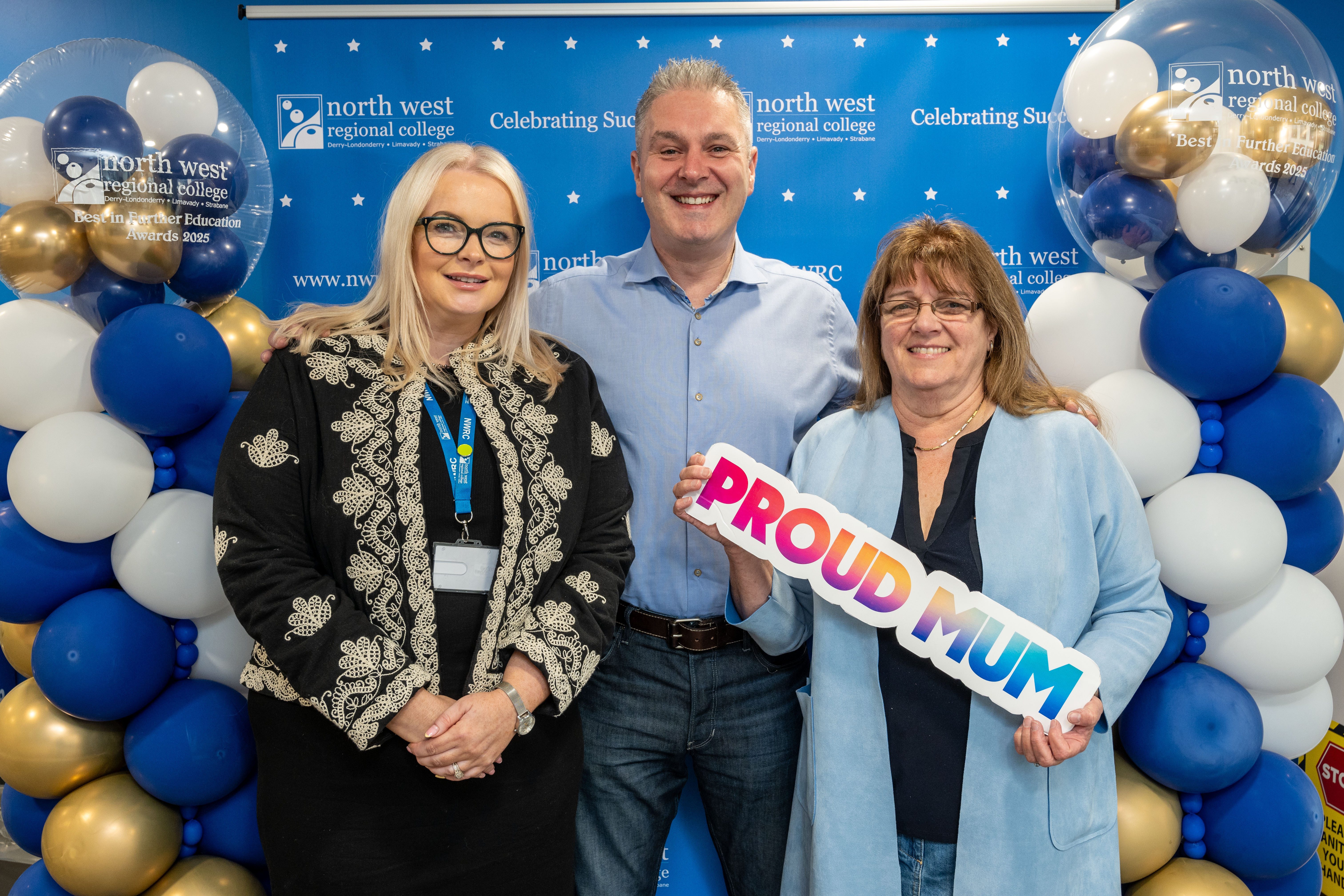 Three people at celebration event. One is holding a sign that says proud mum