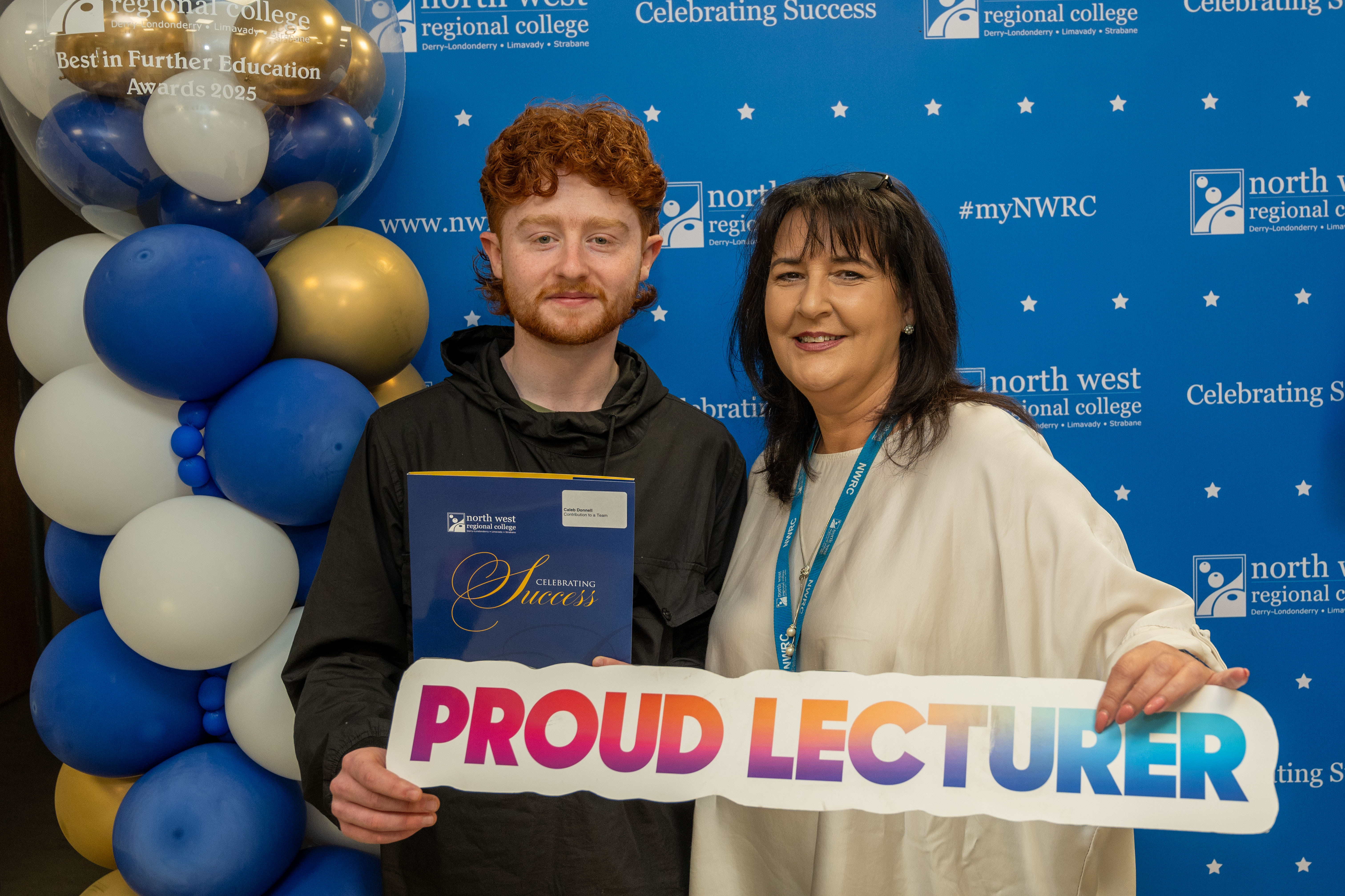 Two people at celebration event. One is holding a sign that says proud lecturer