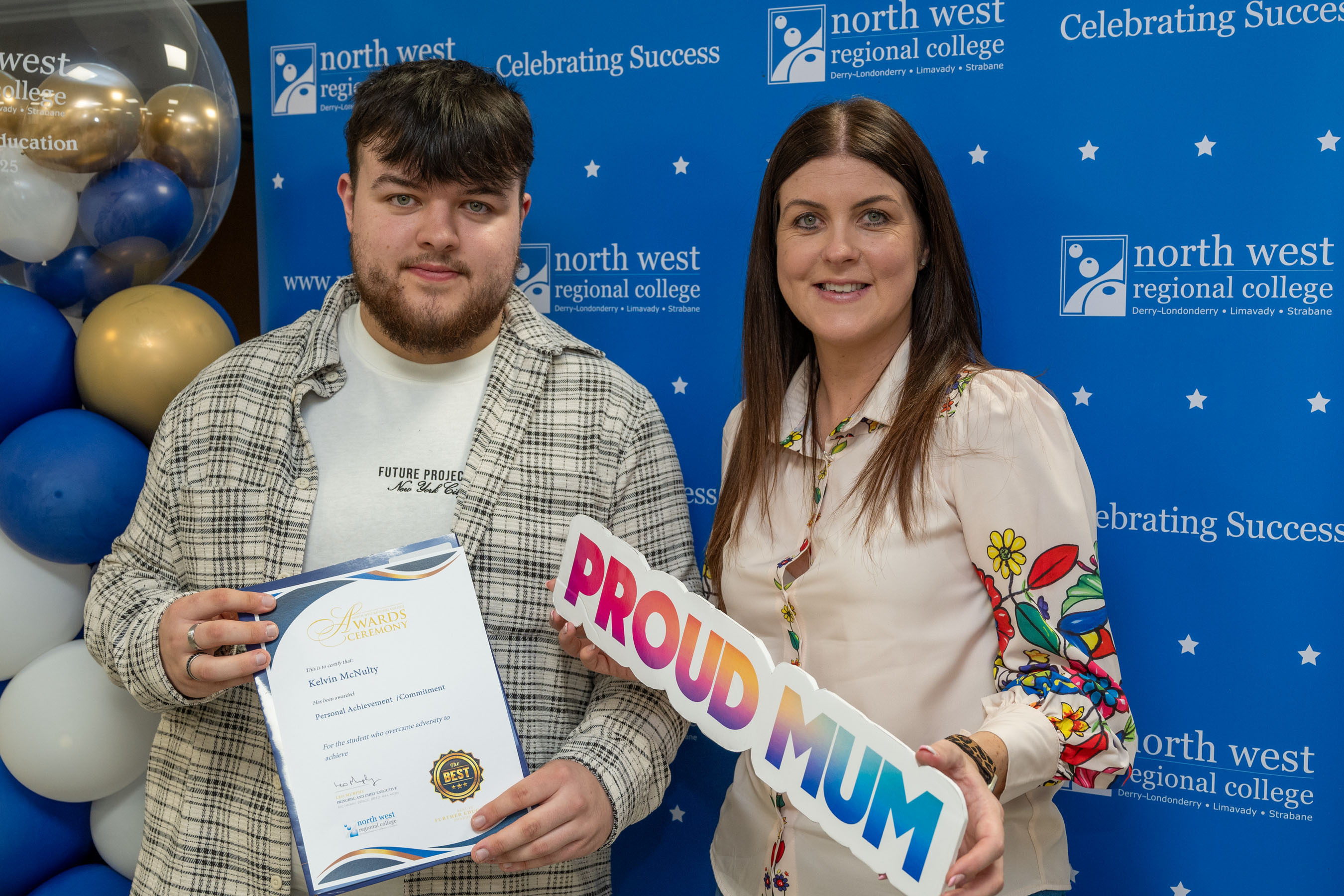 Two people at celebration event. One is holding a sign that says proud mum
