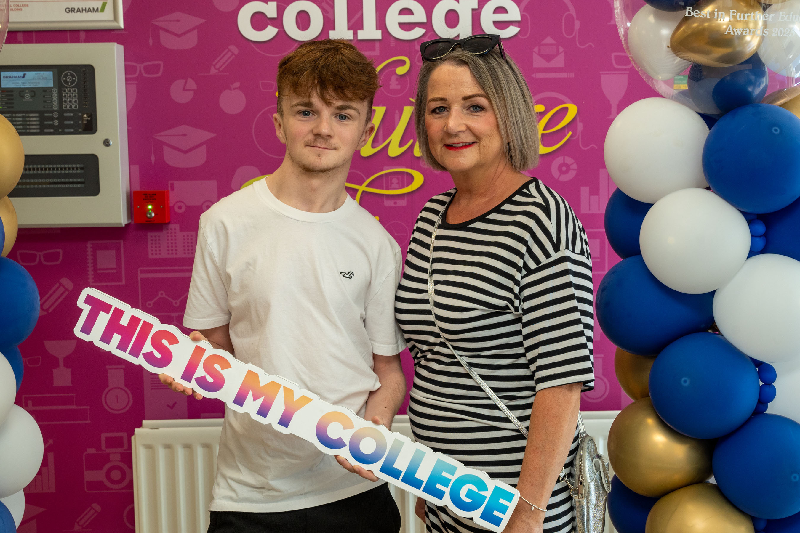 Two people at celebration event. One is holding a sign that says This is my college