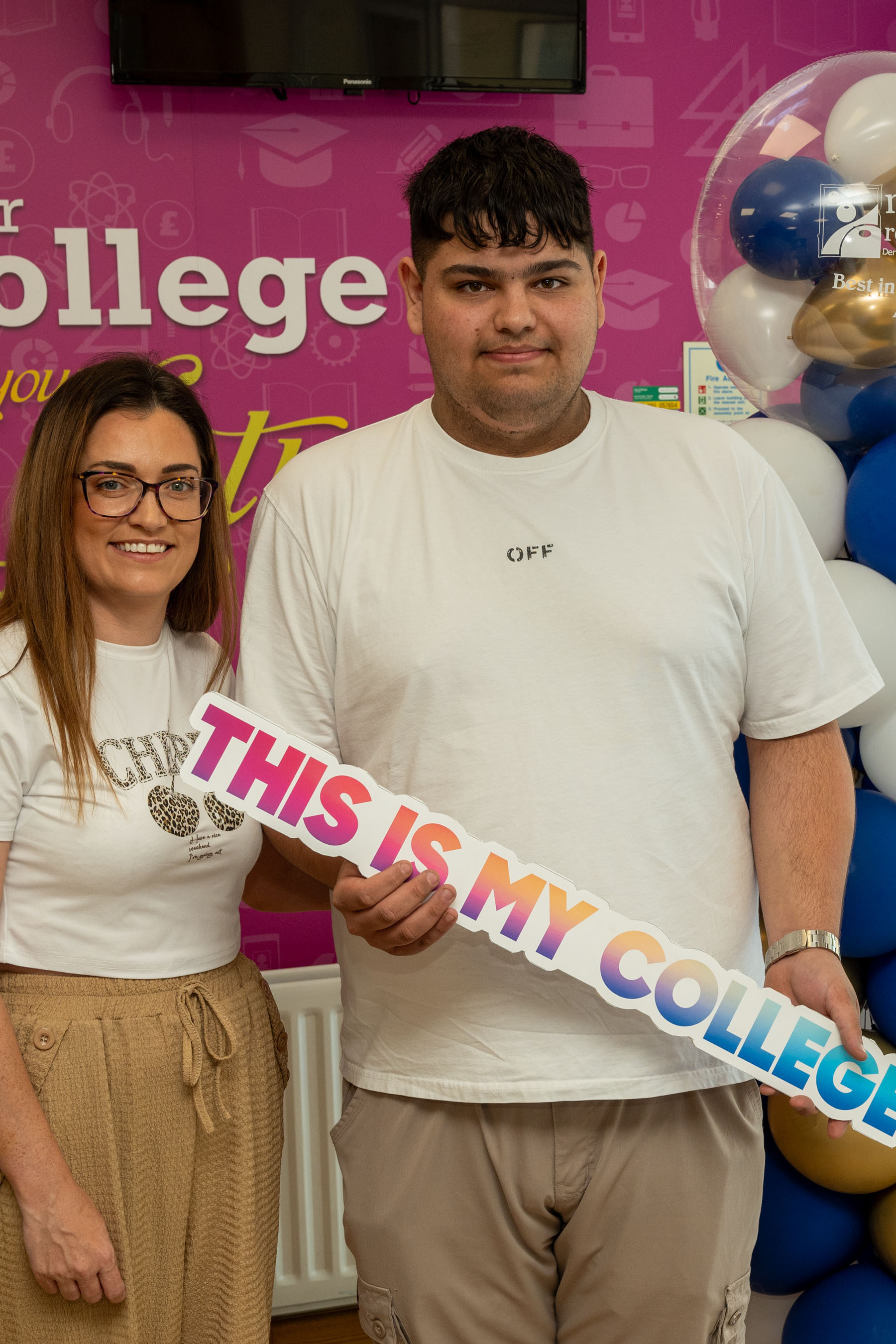 Two people at celebration event. One is holding a sign that says This is my college
