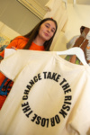 Student holding art work of a  t-shirt which says take the risk or lose the chance