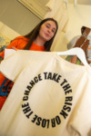 Female student holding art work on a t-shirt which says 'take the risk or lose the chance'