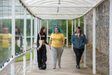 3 female students walking towards the camera in a glass walkway