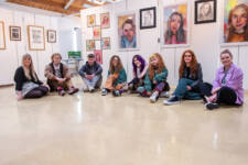 Group of art students sitting with their lecturer in the Art & Design studio with paintings displayed on the walls