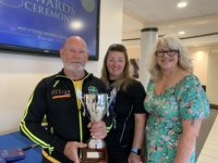 Male and two females holding a trophy inside college building