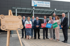 Group of people stand outside college building beside wooden 'Springtown Campus' sign