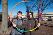 Two studnets pictured outside on a spring morning looking through a hula hoop