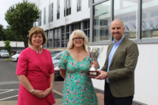 Mature female is presented with award by male and female staff members