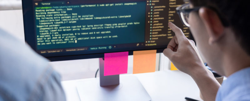 Male points at computer screen with coding displayed on the screen