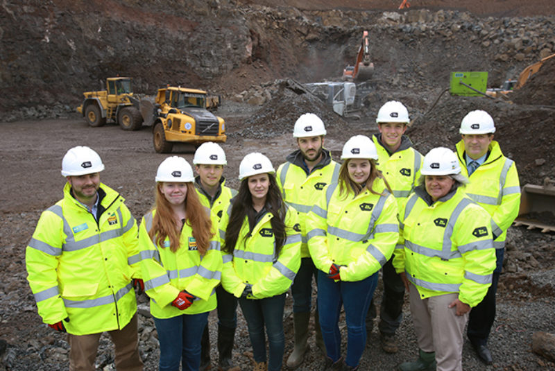 Group of contstruction students on building site wearing high vis jackets and protective helmets