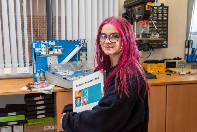 Female Engineering Student with pink hair in Engineering lab holding Process Technology book
