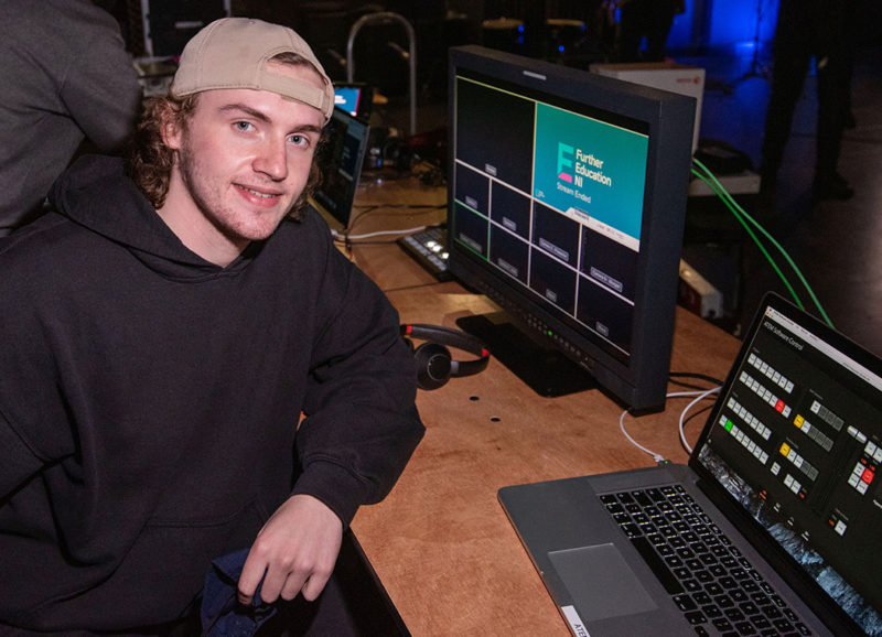 Media Production student Adam Roulston sits in front of a laptop and computer during the live stream of a College event