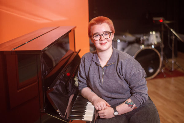 Music student Sarah Jane sits at piano with drums in the background