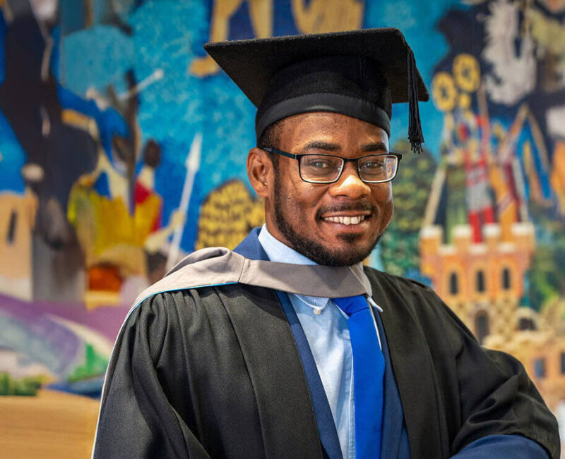 black male graduate smiling with a colourful mural in the background