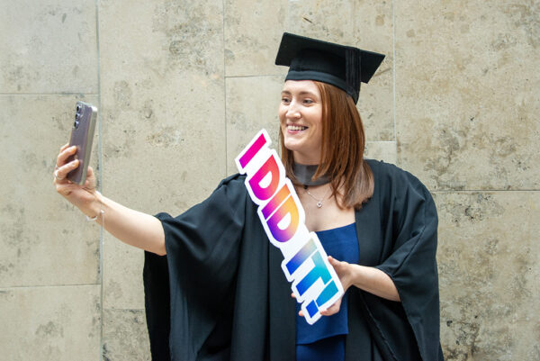 Mature female graduate taking a selfie while holding a 'I DID IT' photo prop