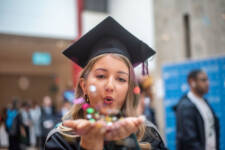 Female Graduate in cap blows glitter towards the camera