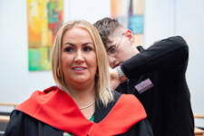 Mature female graduate has gown fitted by staff