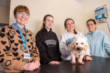 group of four females with a small white dog in college veterinary nursing lab