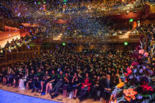 Graduates in auditorium celebrating together as confetti floats down around them