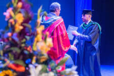 Male graduate recieves his certificate on stage from curriculum manager