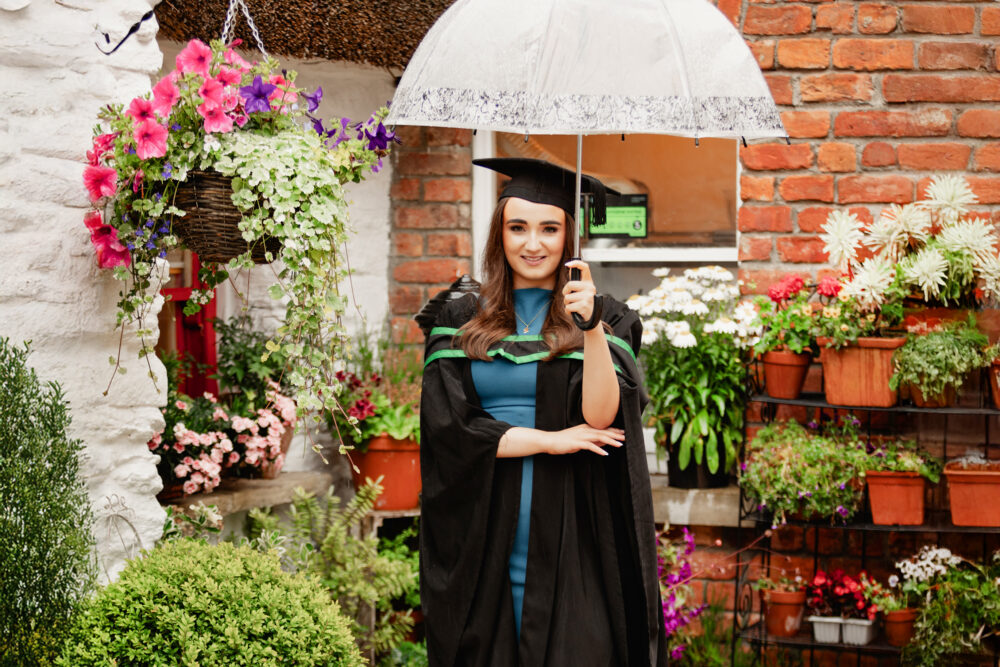 Female graduate with white umbrella, surrounded by flowers and plants