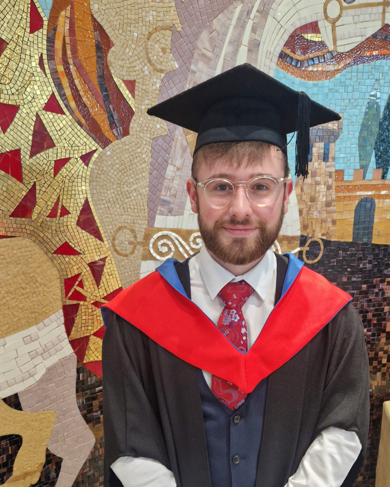 Male graduate smiling while standing in front of a colourful mural