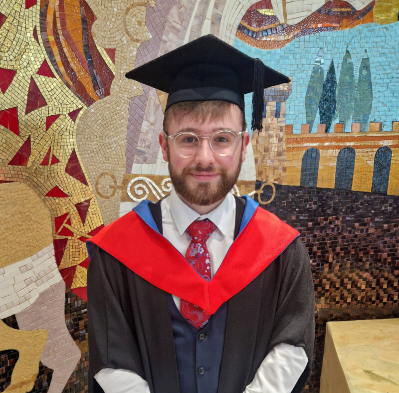 Male graduate stands in front of colourful mural