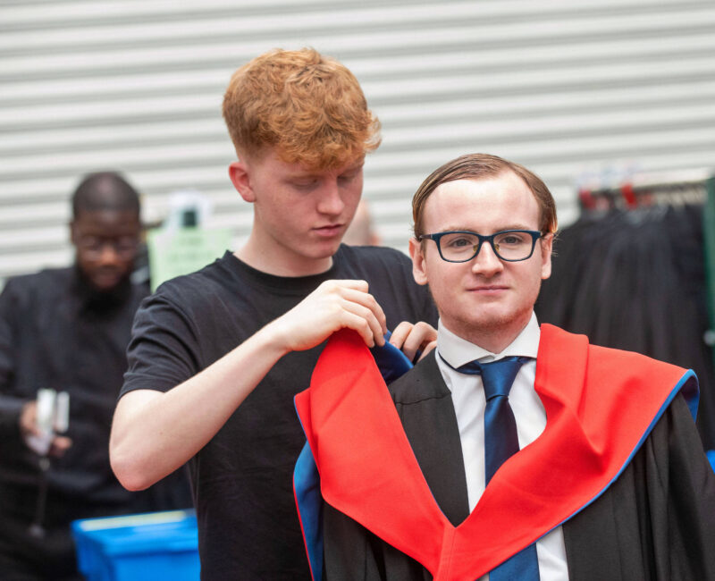 Male graduate has his gown fitted by a member of staff