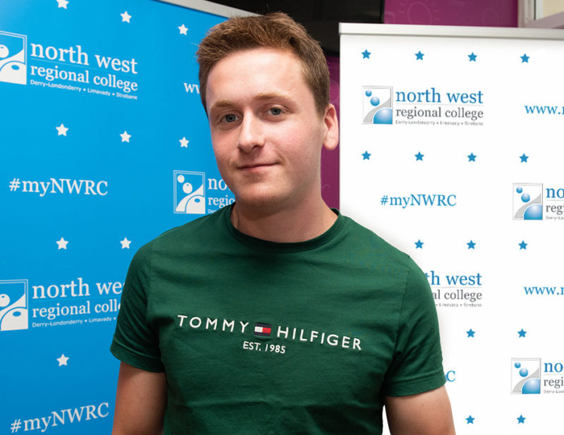 Young man in green Tommy Hilfiger tshirt smiles while standing in front of blue and white NWRC pop-ups