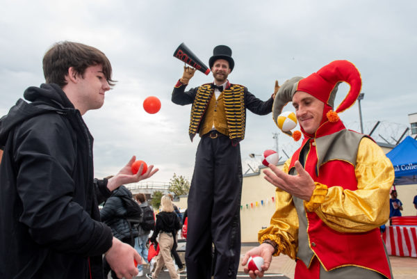 Male student and juggler tossing balls together with a man on stilts behind them at Freshers Day